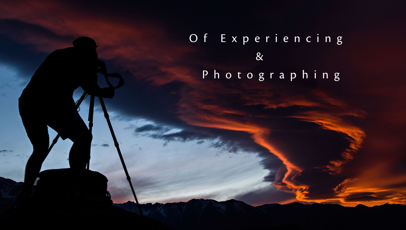 Photographer, camera, and tripod shooting sunset over mountains.