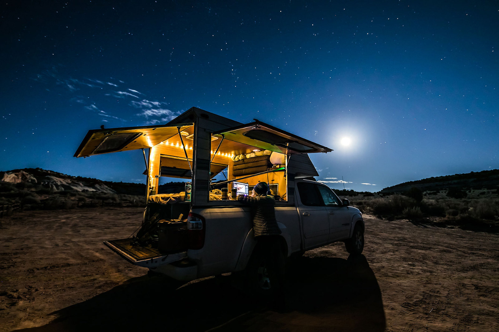 Woman under the stars and moon working on laptop with truck camper.