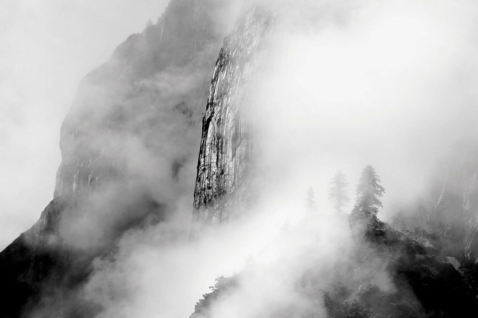 Black & white photograph of a cliff coming out of fog and clearing storm in Yosemite.